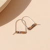 A pair of sterling silver arch earrings with a bar of leopard jasper beads against a neutral background.