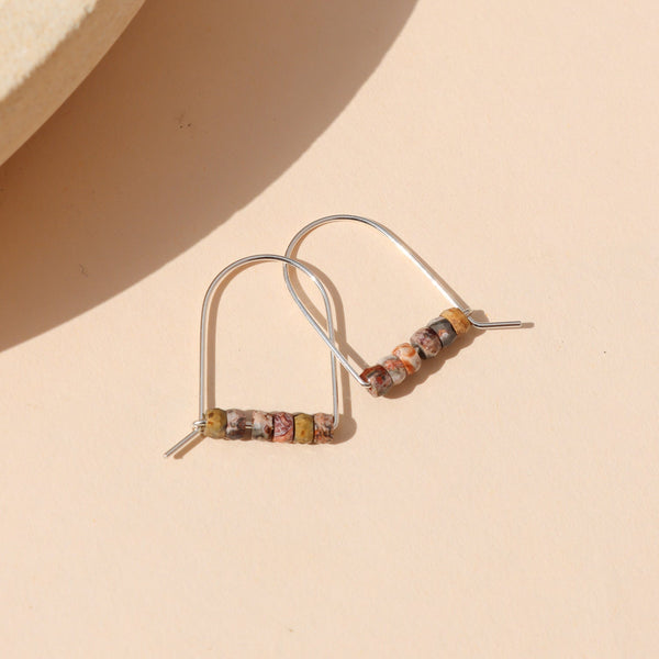 A pair of sterling silver arch earrings with a bar of leopard jasper beads against a neutral background.