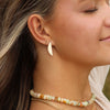 A person with long dark blonde hair wearing a pair of gold silver shaped stud earrings with other jewelry.