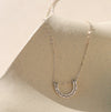 A silver chain necklace with a double U-shaped arch pendant on a shadowy neutral background.