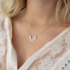 A person with blonde hair and a white shirt wearing a silver chain necklace with a double U-shaped arch pendant.