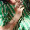 Close-up of a hand with rings and bracelets against a green and white striped background