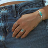 A person with their hand in their jean pocket wearing sterling silver and turquoise rings and bracelet. 