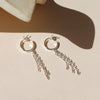 A pair of silver hoop earrings with chain fringe against a shadowy neutral background.