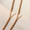 A close view of a woven gold chain necklace laying against a neutral stone backdrop.