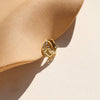 A pair of gold huggie hoop earrings in a braided design, resting against a ceramic shadowy surface.