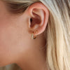 A person with blonde hair wears a braided huggie hoop earring.