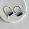 A pair of sterling silver arch earrings with a bar of lapis stone and a lemon jade bead laying against a marble surface. 
