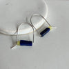 A pair of sterling silver arch earrings with a bar of lapis stone and a lemon jade bead leaning against a marble surface. 