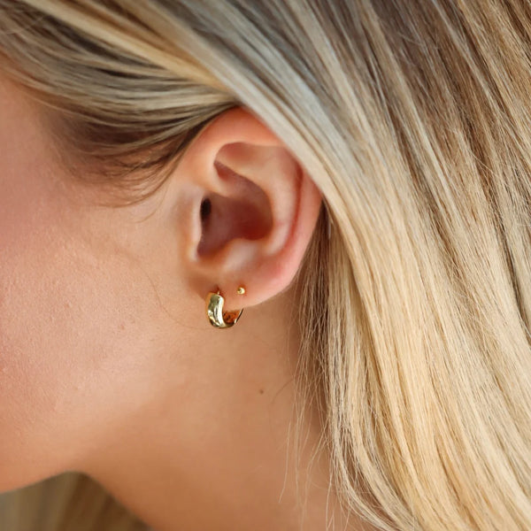 A person with long blonde hair wearing a chunky gold huggie earring stacked with a small gold stud.