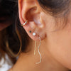 A person with dark hair pulled back, showing their ear stacked with different silver earrings. 