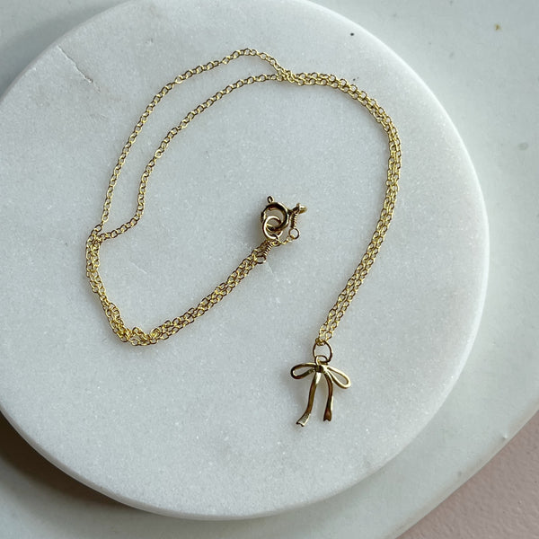 Gold necklace with a bow pendant on a marble surface