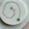Gold necklace with a green gemstone pendant on a white marble surface