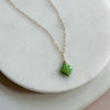 Gold necklace with a green gaspeite stone pendant on a light background