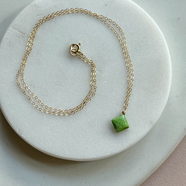 Gold necklace with a green gemstone pendant on a white marble surface