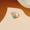 A sterling silver ring with a round turquoise cabochon stone, displayed on a minimalist beige and orange surface with a ceramic plate edge in the background.