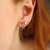 Close-up of an ear wearing a silver wishbone stud earring with a heart-shaped stud.