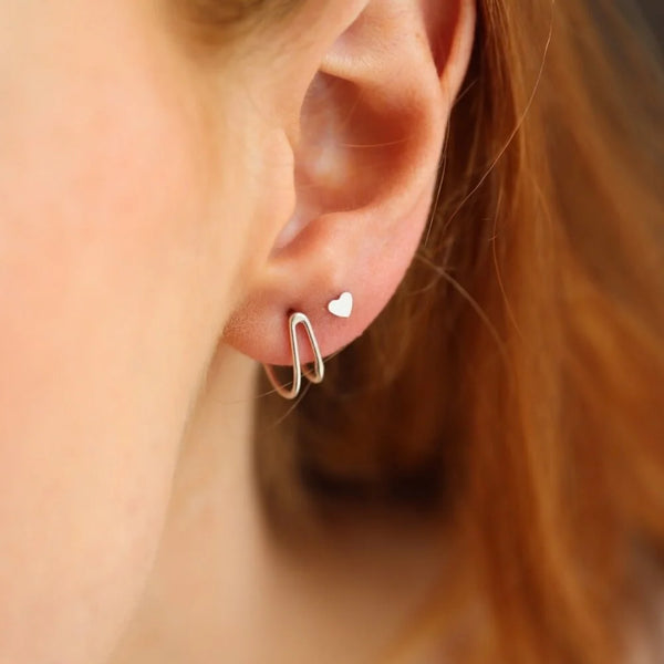 Close-up of an ear wearing a silver wishbone stud earring with a heart-shaped stud.