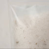 A clear plastic resealable pouch containing white soaking salts with bits of dried white sage, photographed against a plain light background.