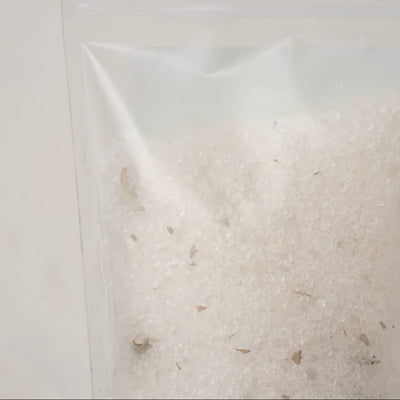 A clear plastic resealable pouch containing white soaking salts with bits of dried white sage, photographed against a plain light background.