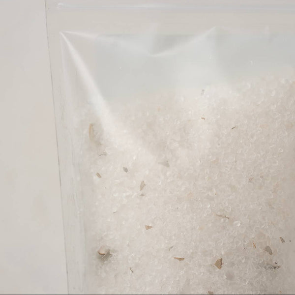 A clear plastic resealable pouch containing white soaking salts with bits of dried white sage, photographed against a plain light background.