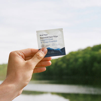 Hand holding a Ursa Major essential face wipe with a blurred natural background