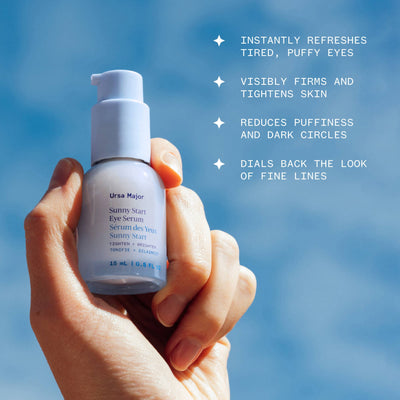 Hand holding a bottle of Ursa Major Sunny Start Eye Serum with a blue sky background