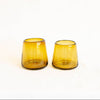 Two small amber handblown glass tumblers with a tapered shape, standing side by side on a plain white background.