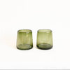 Two small translucent olive green handblown glass tumblers on a plain white background.