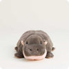 A plush hippopotamus toy lying down, featuring dark gray plush fur, small pink inner ears, and a soft pink under-chin and mouth area, set against a plain off-white background.