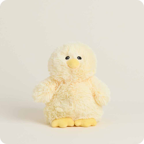 A soft plush toy chick with fluffy pale yellow fur, a bright yellow beak, and bright yellow feet, centered against a warm off-white background.