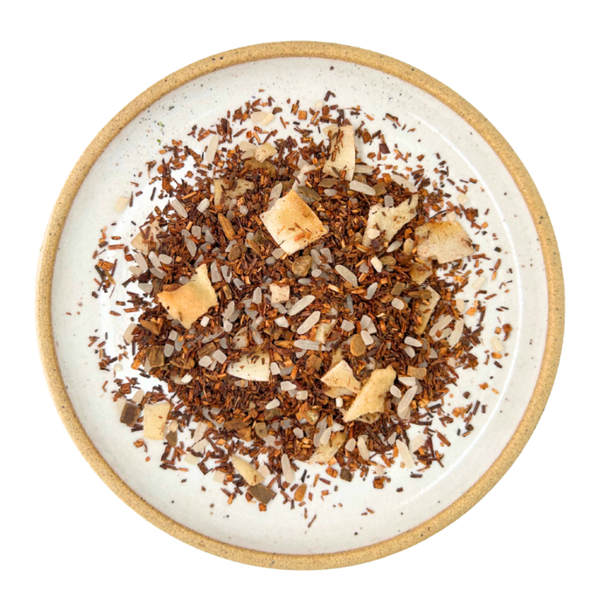 A top-down view of loose-leaf herbal tea  on a round speckled ceramic plate with a beige rim, set against a solid white background.