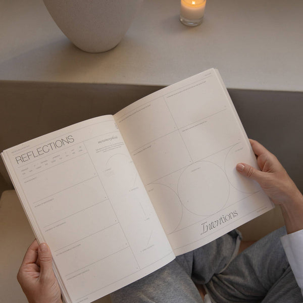 Person holding a notebook titled 'Reflections' with a candle and vase in the background.
