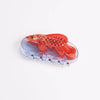 A translucent clear claw hair clip featuring a bright red-orange fish design inlaid with sparkles, photographed on a clean white background.