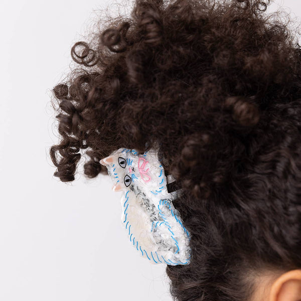 Close-up of a person with curly hair wearing a decorative white cat hair clip on a white background