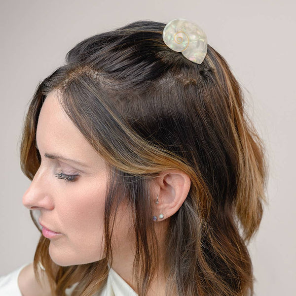 Woman with styled hair featuring a decorative shell-shaped hair clip against a plain background