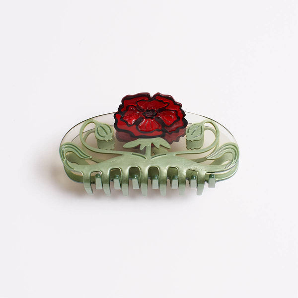 A clear acrylic hair claw clip featuring a light green scrollwork base and a prominent red poppy flower on top, photographed on a clean white background.