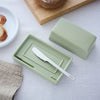 Green butter dish with a silver knife on a light surface with bread in the background
