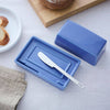 Blue butter dish with a knife on a table with bread in the background