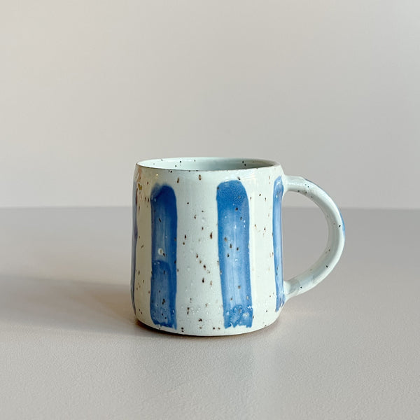 A ceramic espresso mug in a white speckled glaze with blue brushstroke stripes, against a neutral backdrop.